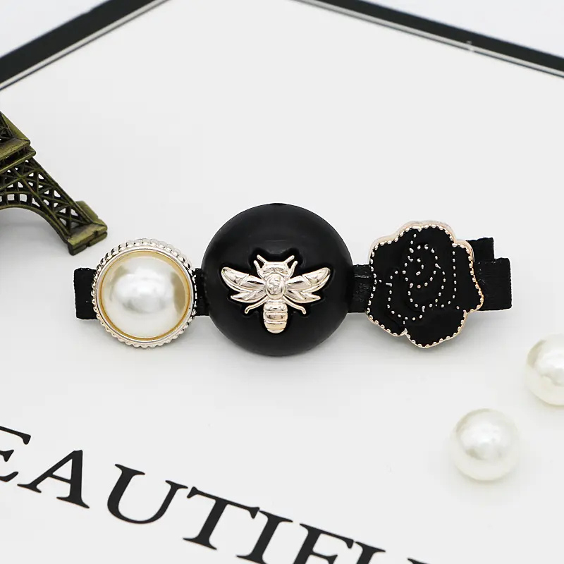 Decorative hair clip with black center, pearl on one side, bee emblem, and flower